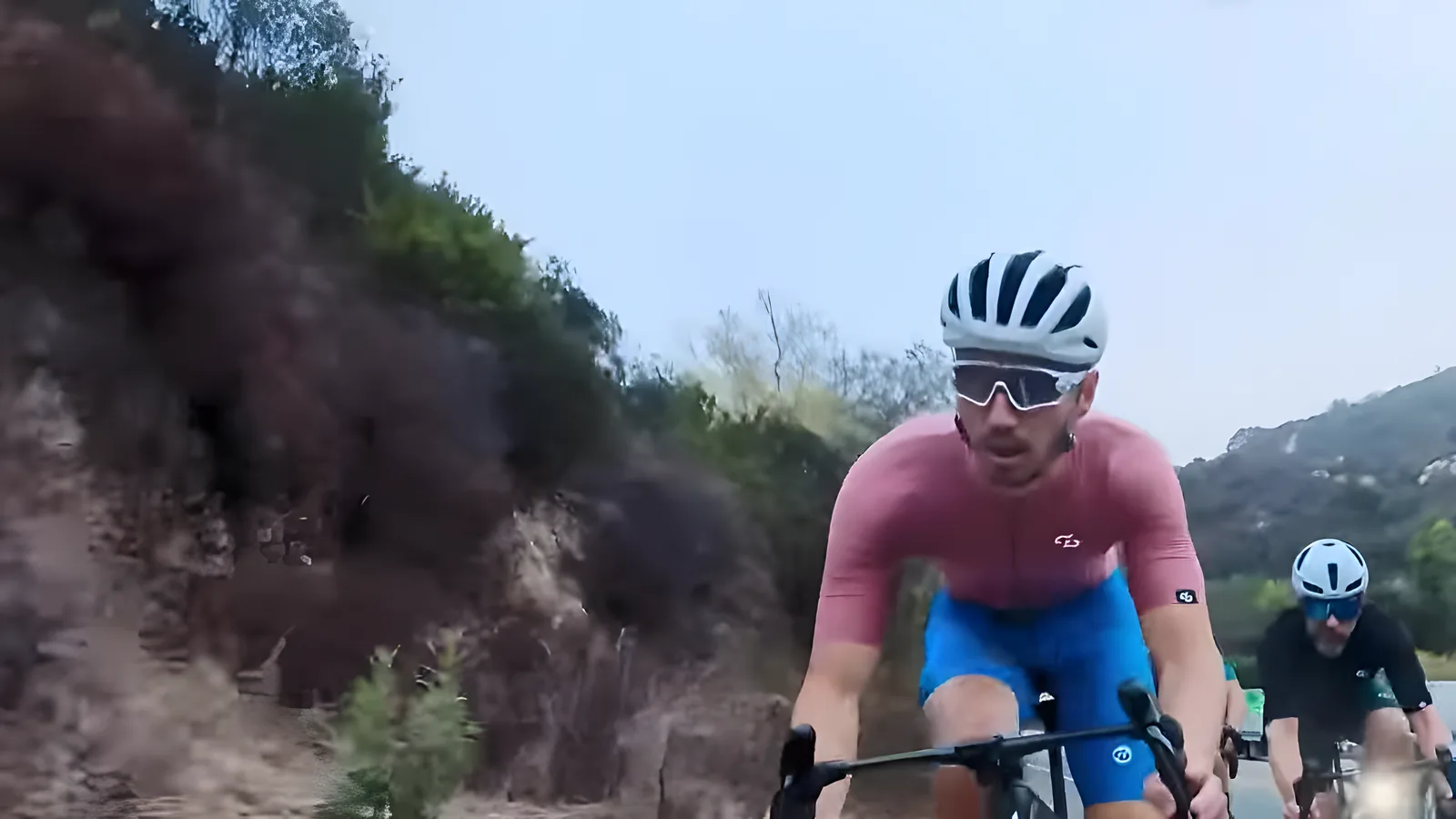 Bus Stop rider in a pink jersey climbing a canyon road with hills behind